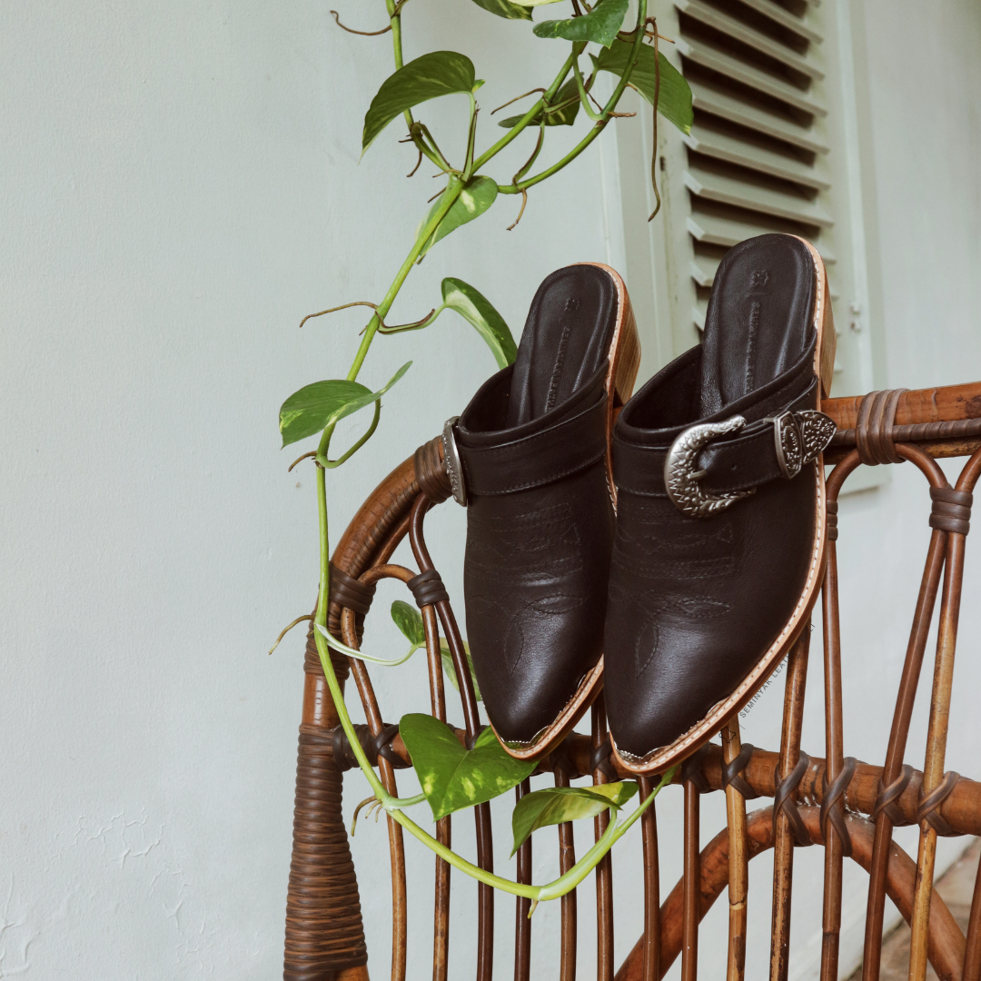 a pair of KARMA cowboy mule heels in black color hang on the chair, the  mule heels is made of genuine sheep leather upper, leather sole, and 5 cm wooden heels